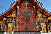 Wat Xieng Thong temple in Luang Prabang, Laos. The back wall with its famous tree of life mosaic in colored glass on a dark red background.  